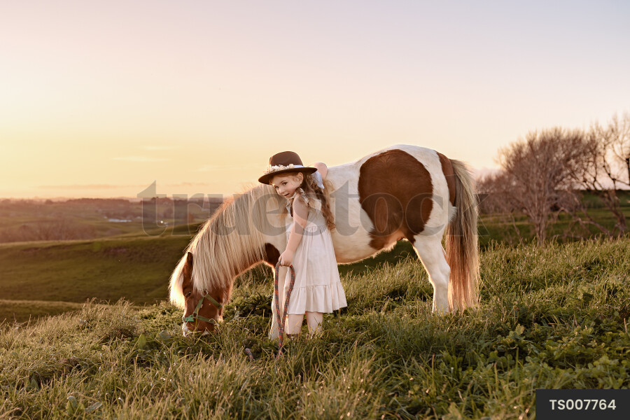 Girl with pony in field at sunset