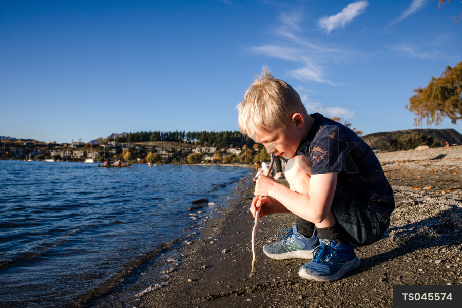 Boy crouching with stick by lake