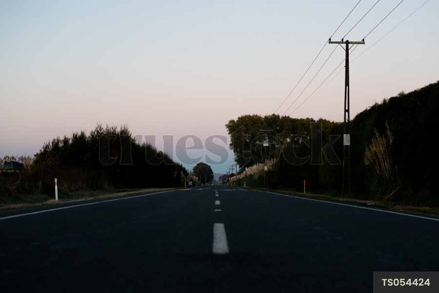 Road under power lines through countryside during sunset