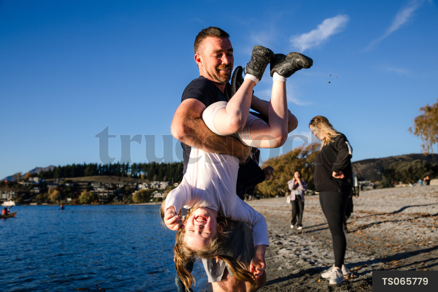 Father carrying daughter upside down by lake