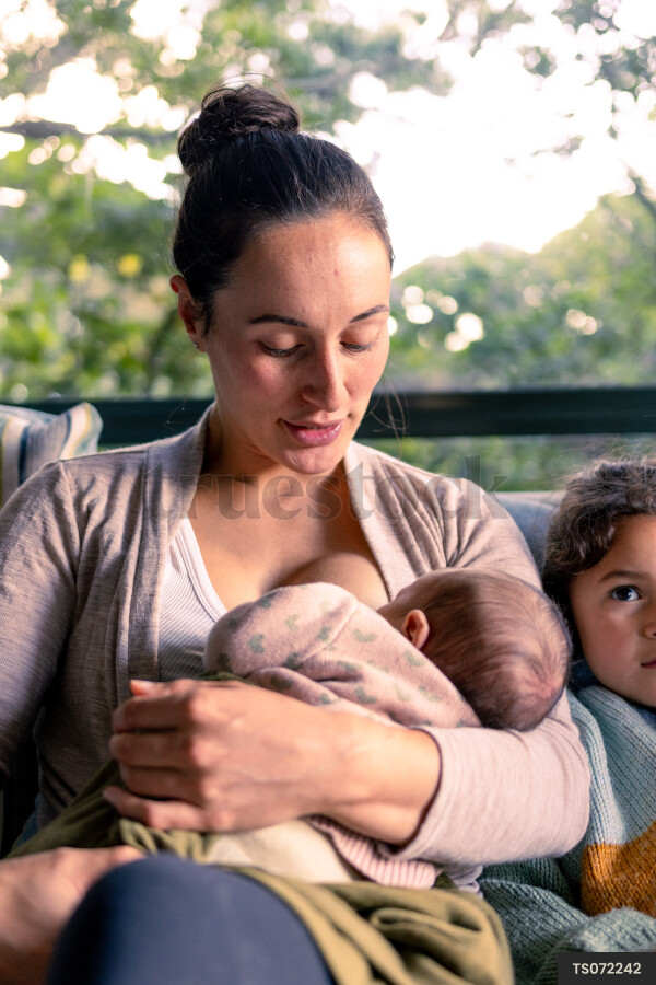 Mother breastfeeding newborn daughter with niece in living room