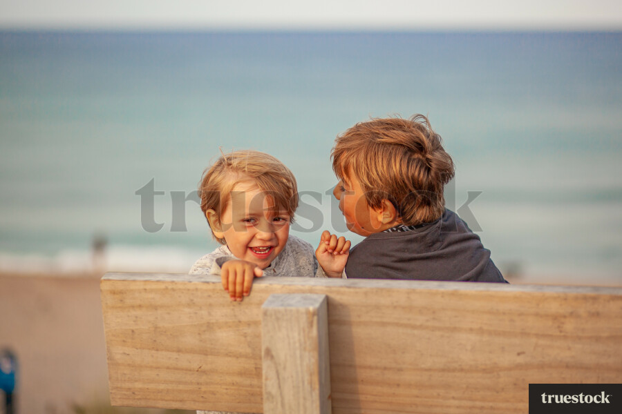 Children smiling and sitting on a picnic bench at the beach