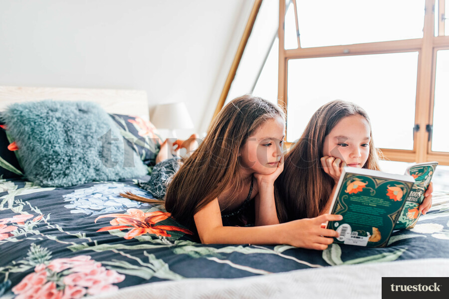 Twin Sisters Reading Book on Bed