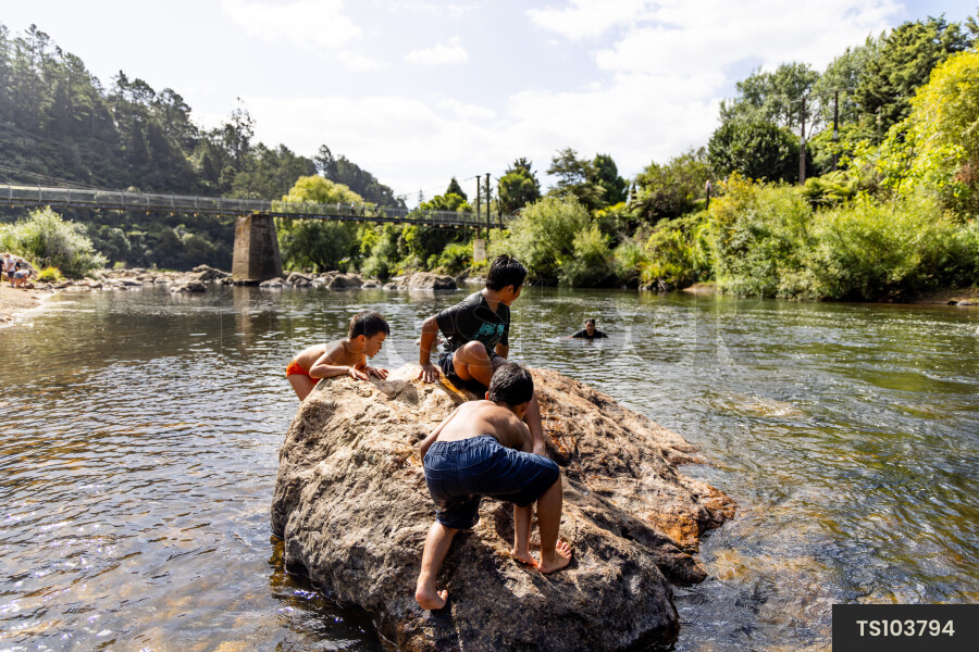 Boys playing on rock by river