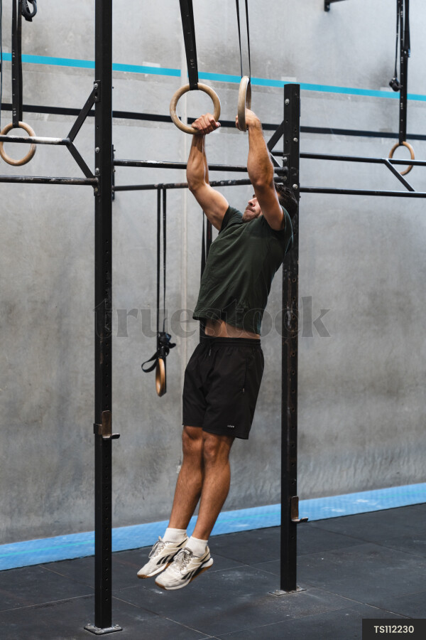 Young man hanging on gymnastics equipment in gym