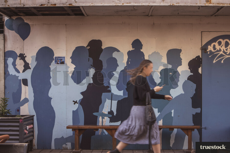 Female adult general public walking past street art mural on her phone