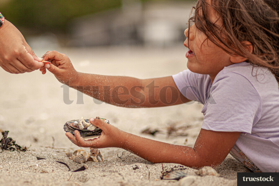 Child lying in the sand with collection of shells