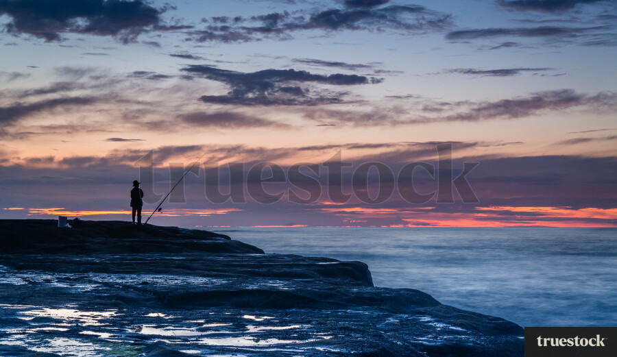 Fisherman fishing off the rocks at sunset