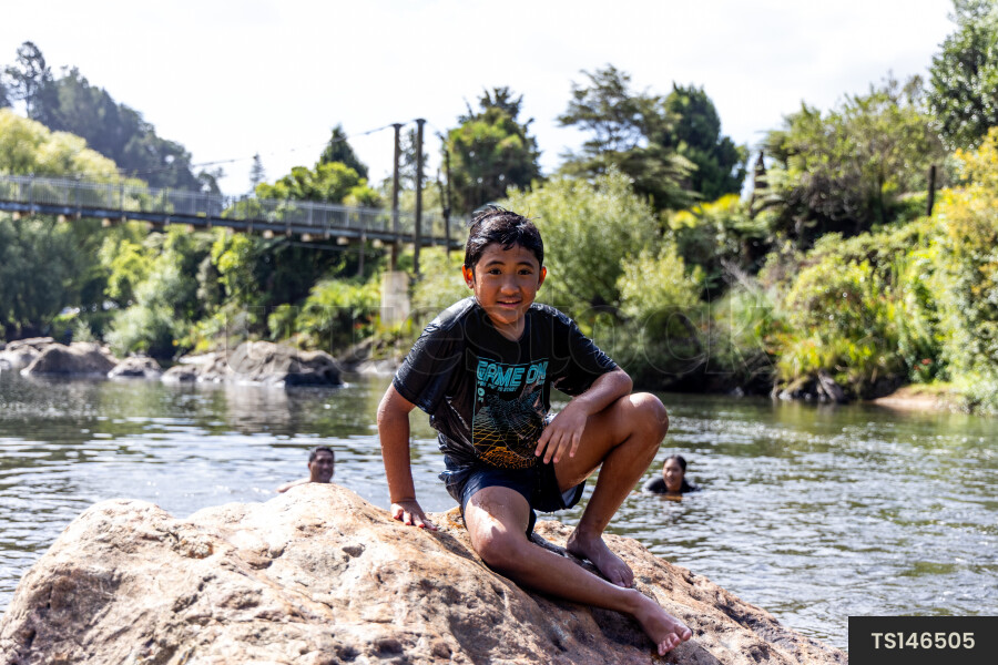 Boy sitting on rock by river