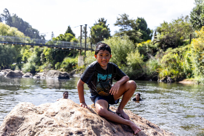 Boy sitting on rock by river