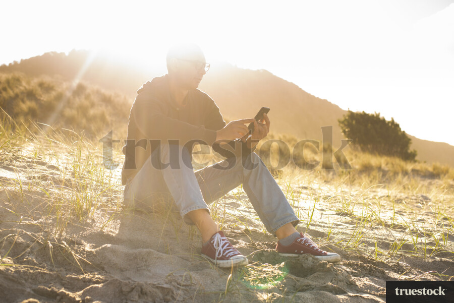 Male on beach with mobile phone under sunlight