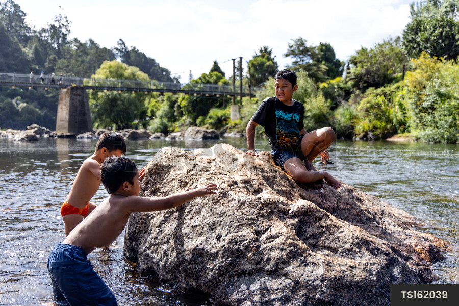 Boys playing on rock by river