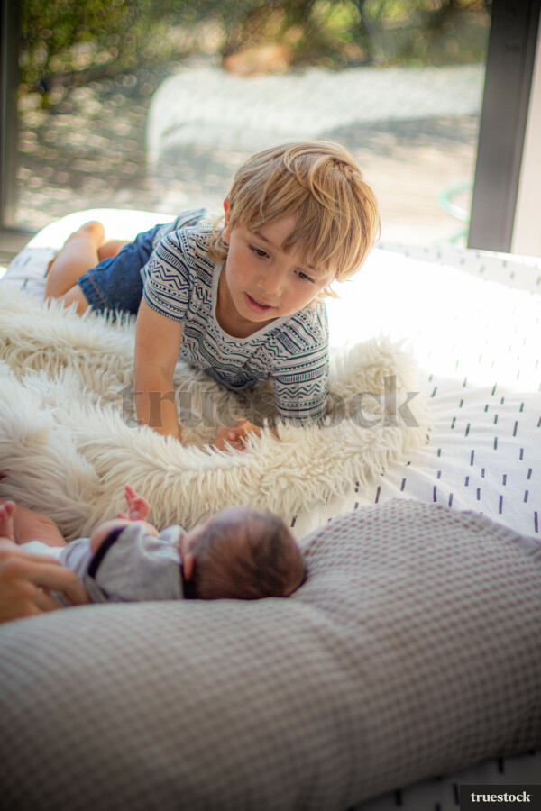 Big brother lovingly watching his baby brother lying on the bed