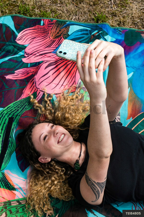 Young woman taking selfie while lying down on picnic blanket