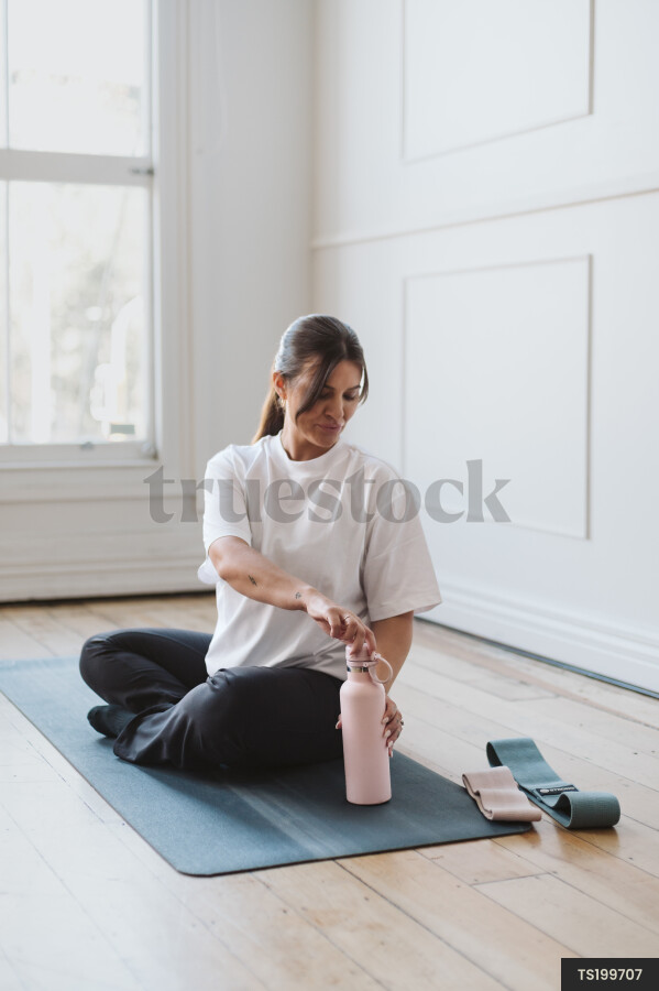 Woman sitting exercise mat opening water bottle