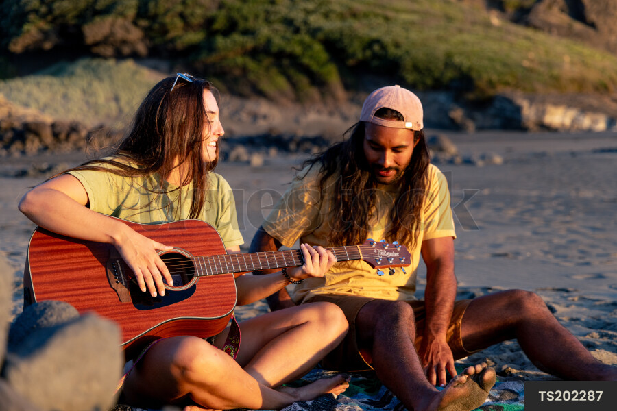 Couple with guitar on beach at sunset