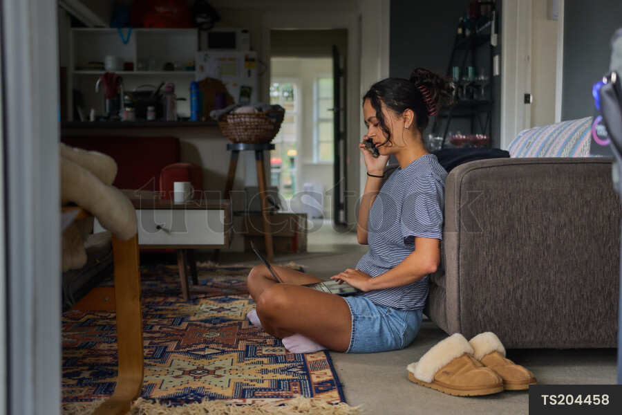 Young woman talking on smart phone sitting on lounge floor