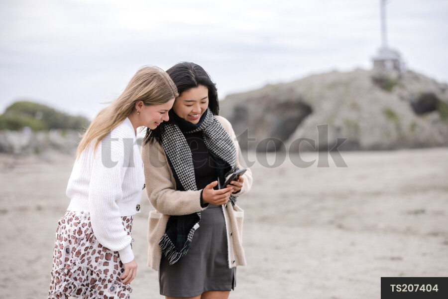 Happy friends looking down at cell phone on beach