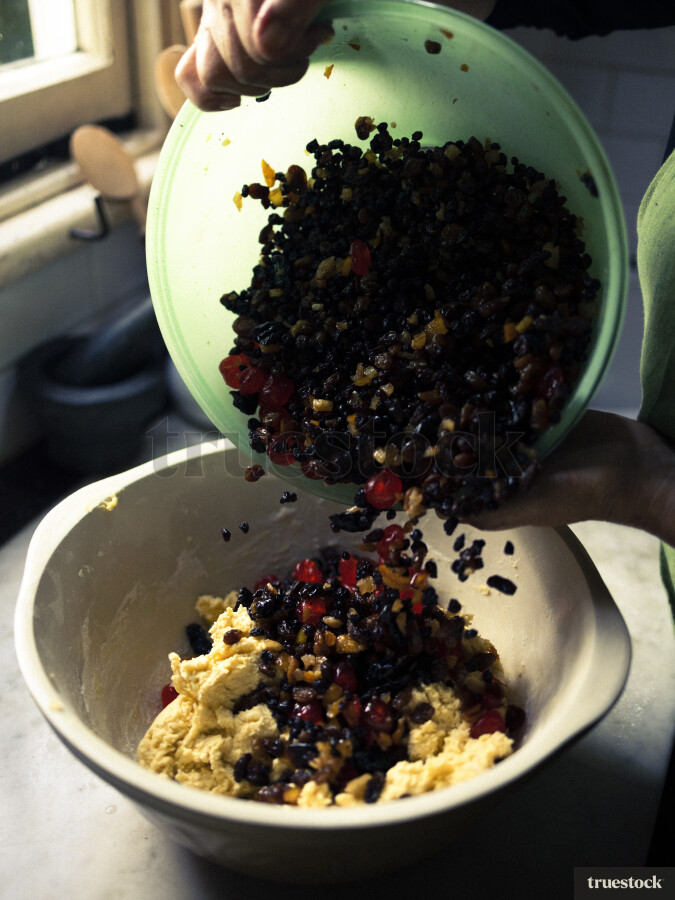 Person Pouring Fruit and Nuts into Batter
