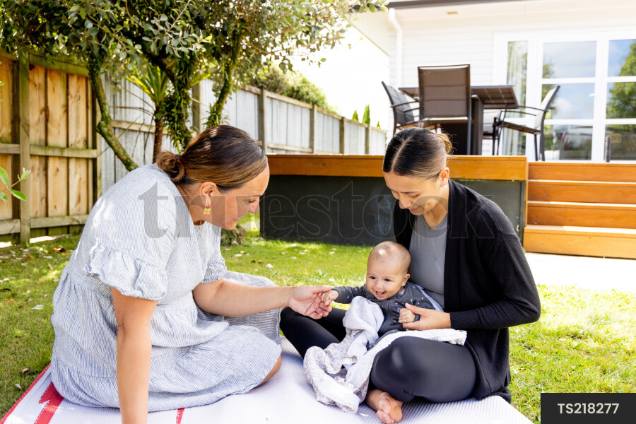 Mother and grandmother with baby boy on picnic blanket