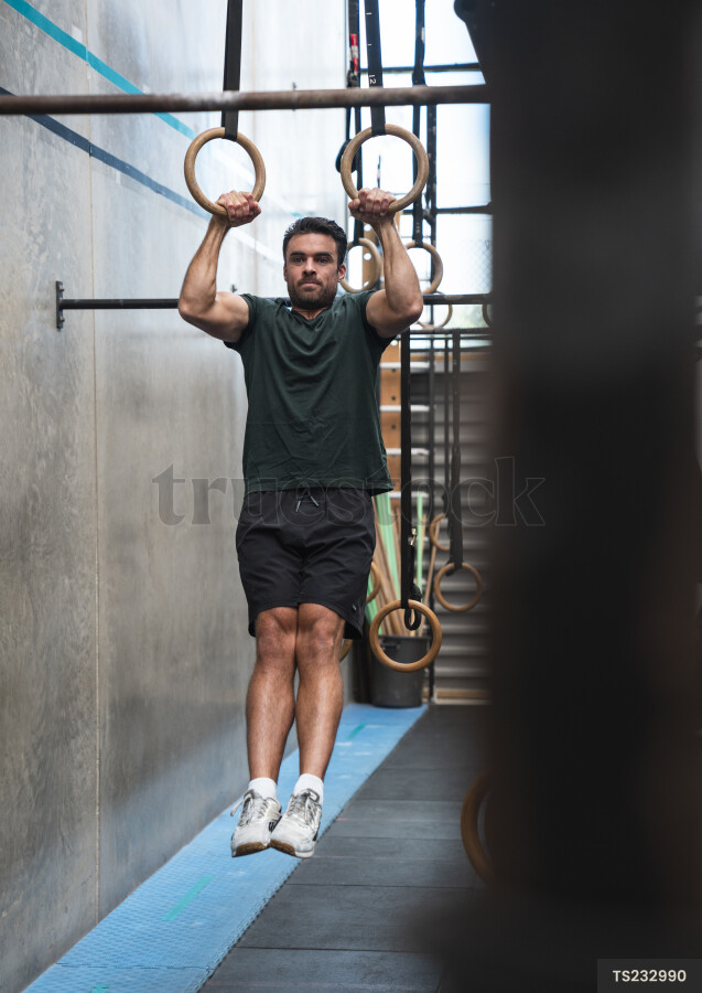 Young man hanging on gymnastics equipment in gym