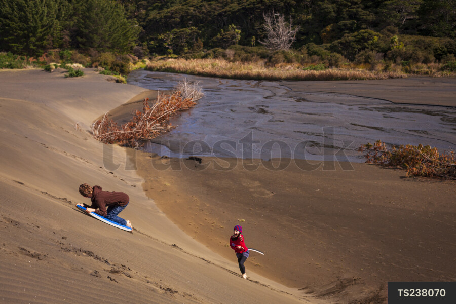 Children playing on sand dunes at Bethells Beach