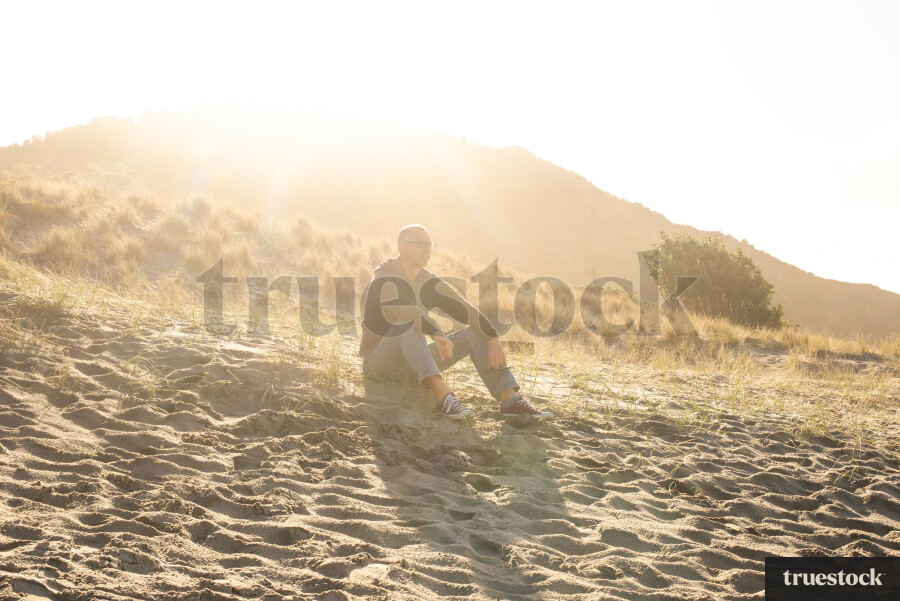 Adult sitting on the sand at the beach with sunbeams