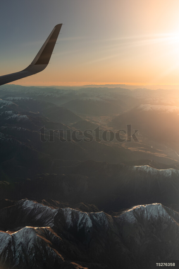 Wing of airplane flying over mountains at sunset