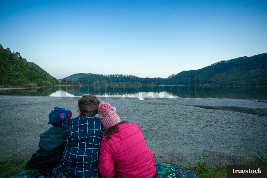 Siblings sitting together on picnic blanket by the lake in the evening