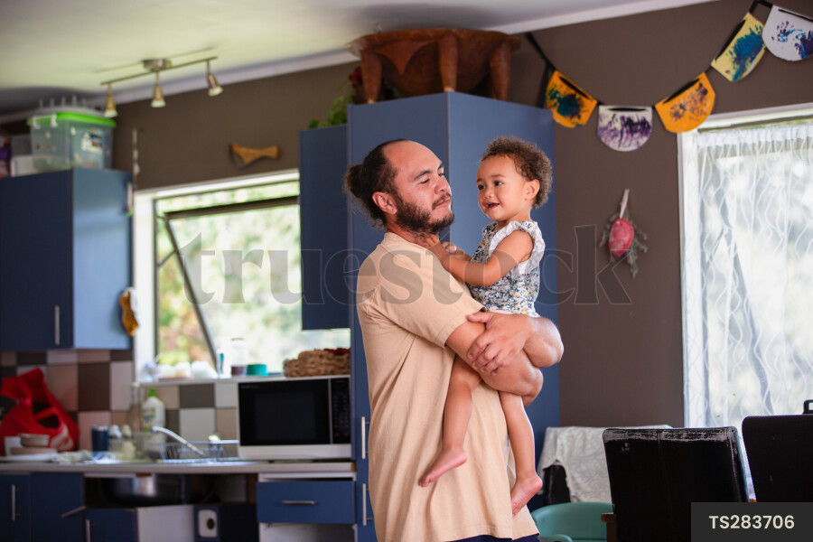 Maori dad carrying daughter in kitchen of home