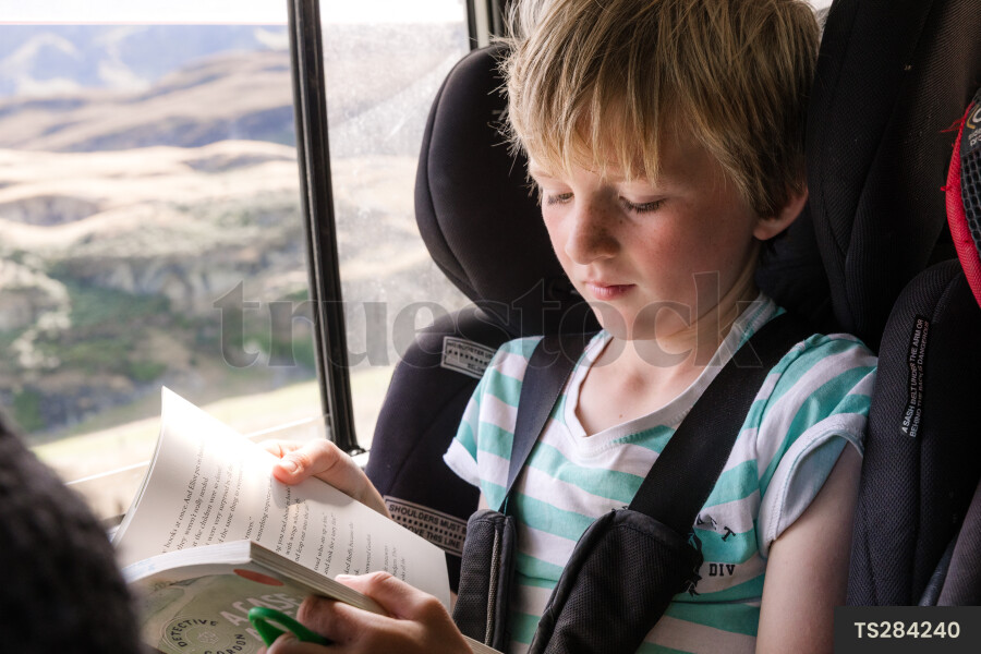 Boy reading book in car on road trip in national park