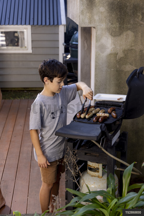 Boy cooking sausages on barbecue grill in garden