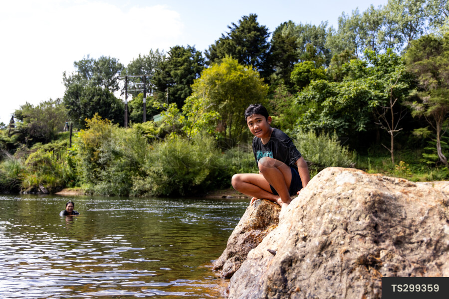 Boy sitting on rock by river