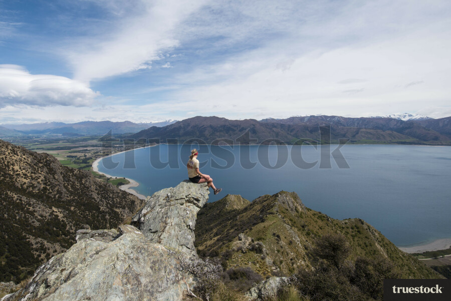 Female adult sitting on the edge of a cliff rock on top of the mountain overlooking the lake