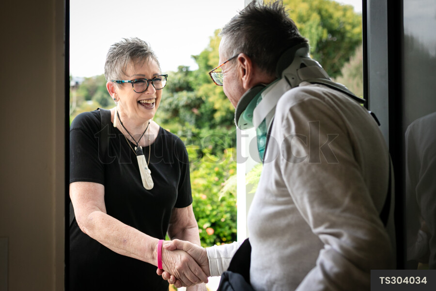 Health carer and patient shaking hands at front door