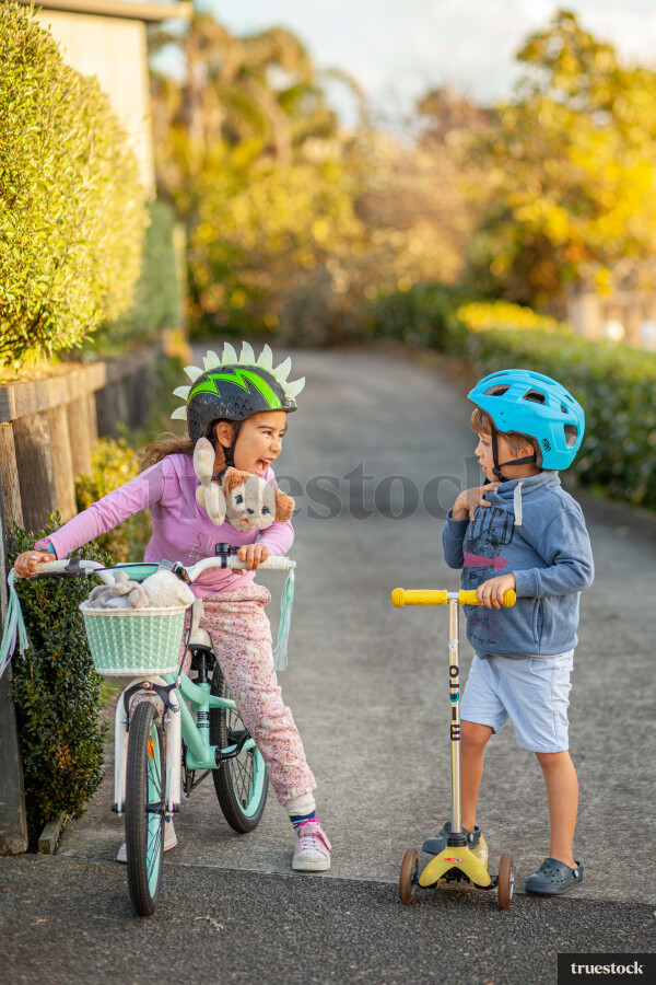 Siblings riding their bike and scooter down the street pathway