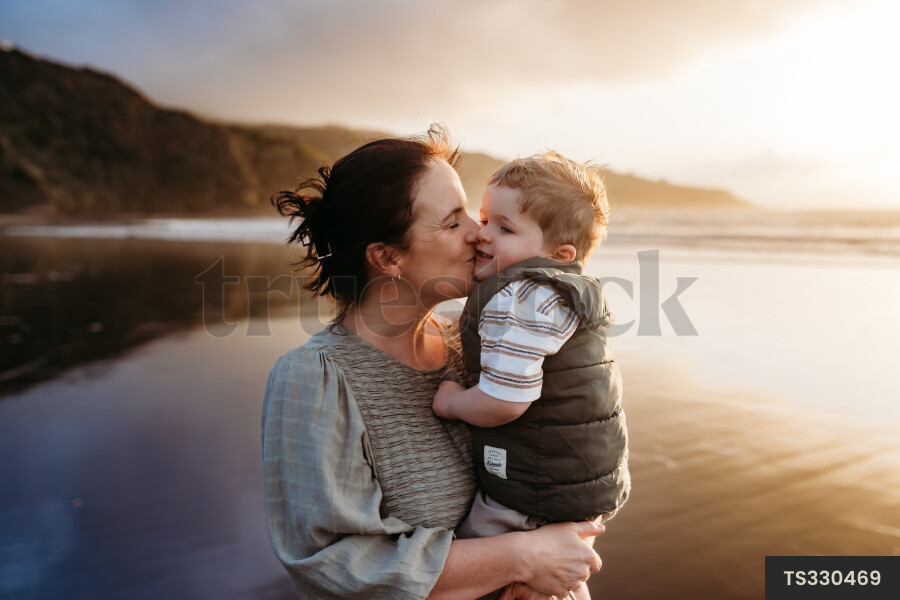 Mother embracing son on beach during sunset