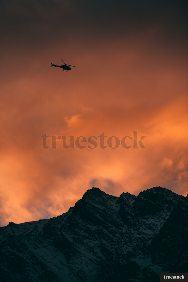 Helicopter flying over mountain peak during sunset