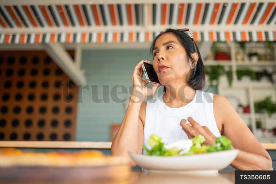 Asian woman talking on smart phone over lunch in house