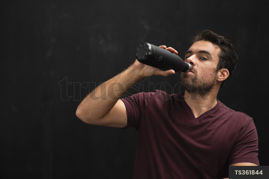 Young man drinking water out of bottle in gym