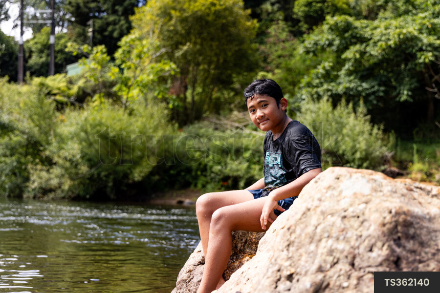 Boy sitting on rock by river
