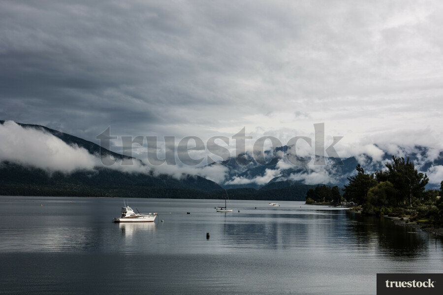 Low hanging clouds over mountains with boats in the lake