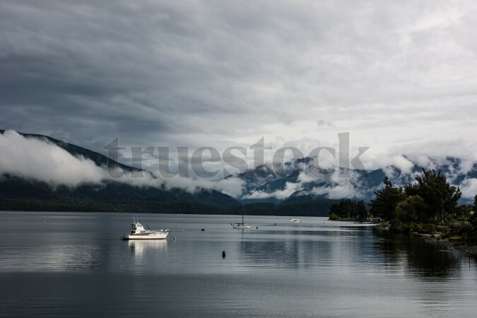 Low hanging clouds over mountains with boats in the lake