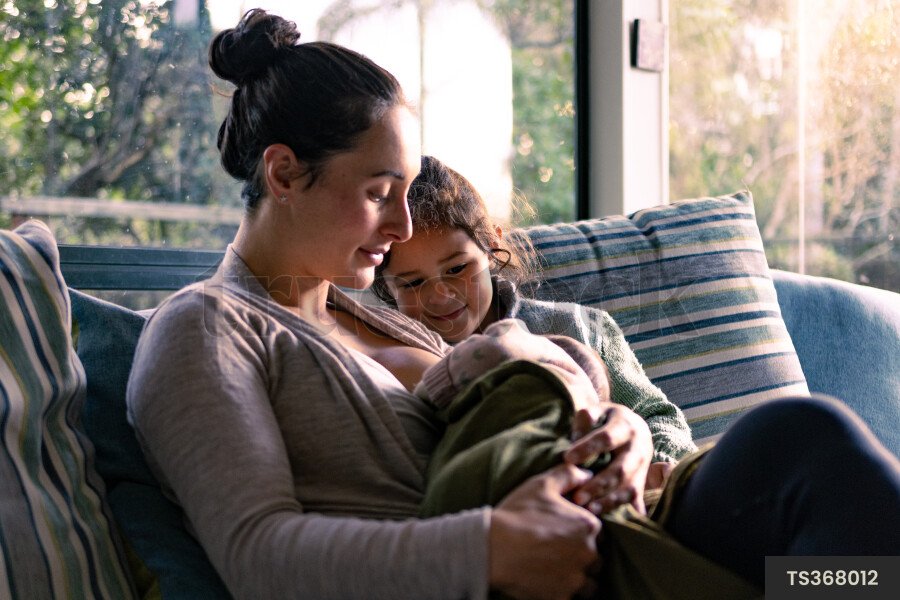 Mother breastfeeding newborn daughter with niece in living room