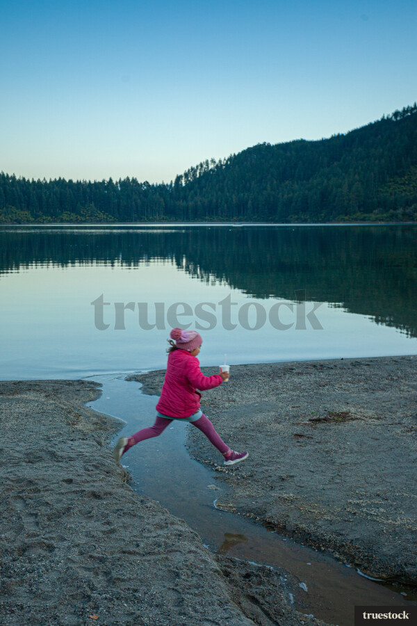 Child running and jumping over water creek by the lake