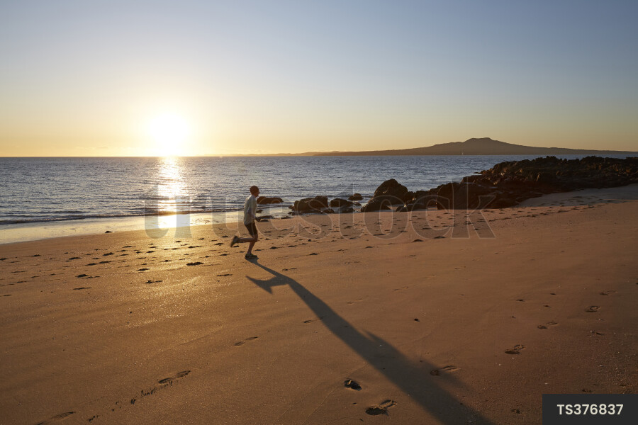 Man jogging on beach at sunrise in Auckland