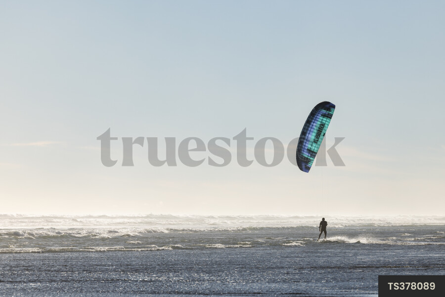 Silhouette of man kitesurfing on waves in sea