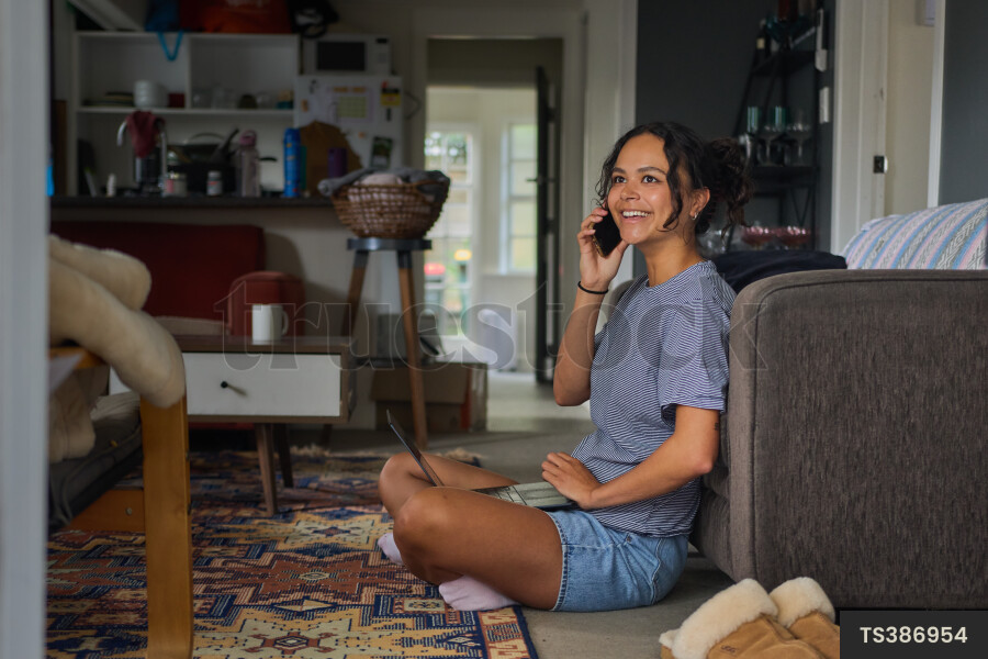 Young woman talking on smart phone sitting on lounge floor