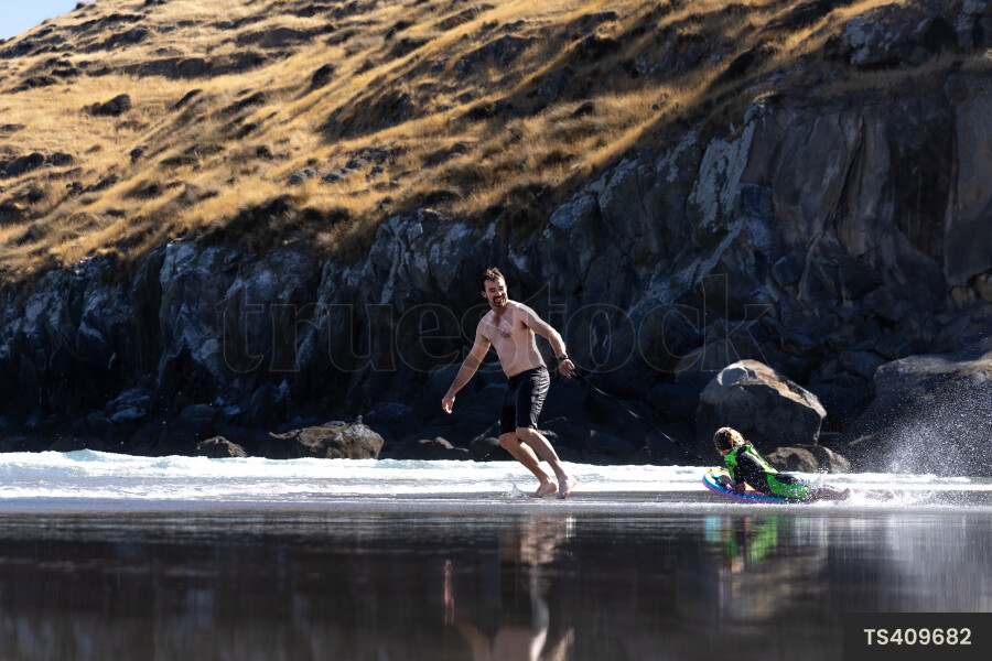 Father and son playing with boogie board on beach