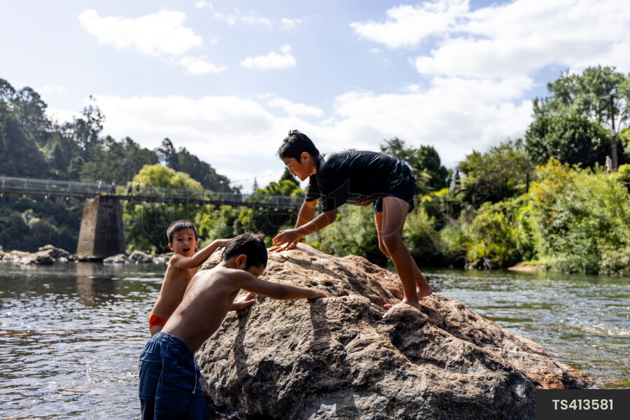Boys playing on rock by river